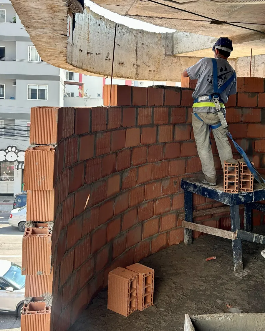 Colaborador de capacete e cinto de segurança executando alvenaria de fechamento externo