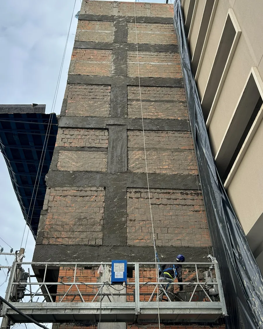 Fachada de edifício em execução, com balancim suspenso e colaborador trabalhando