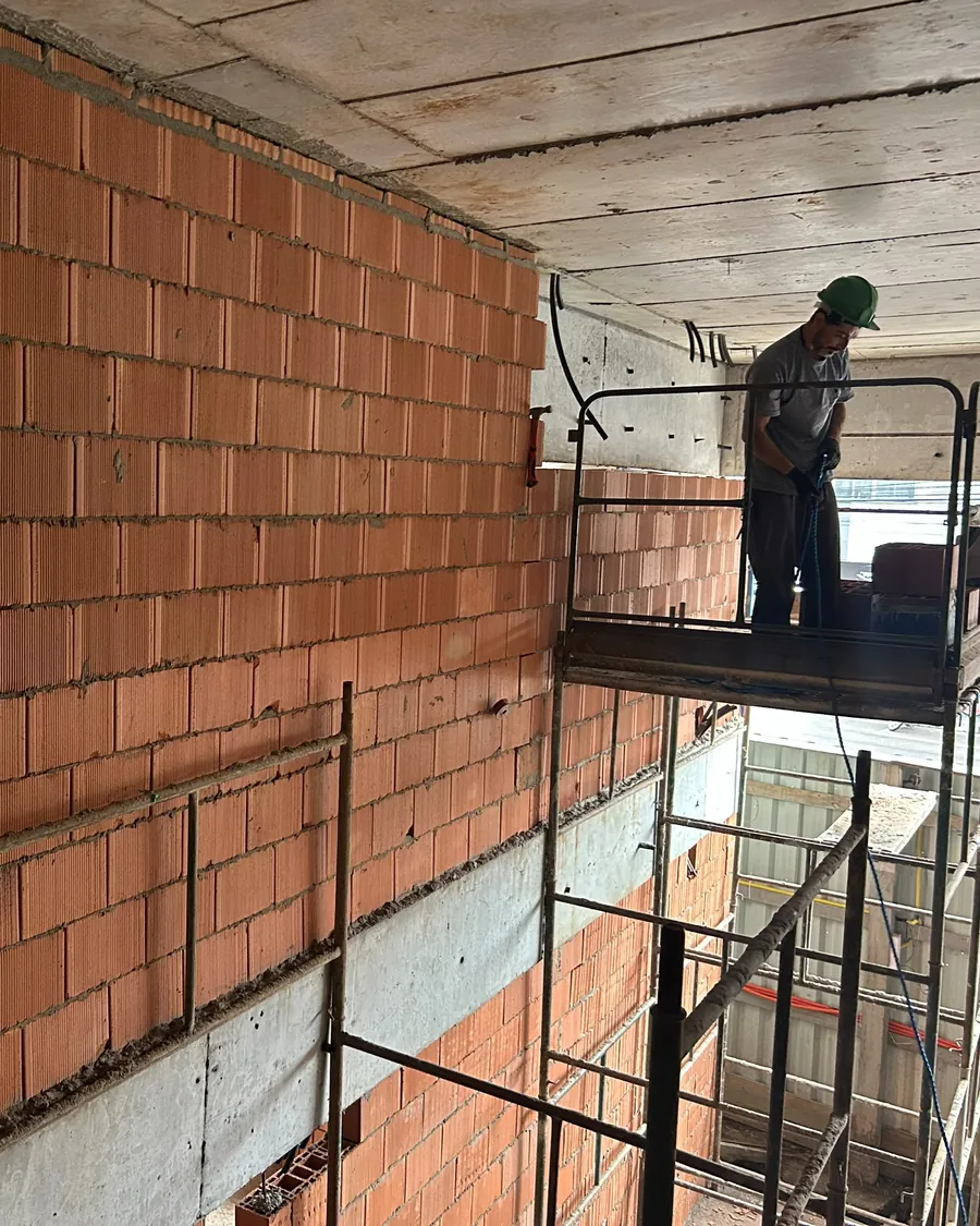 Colaborador executando alvenaria em altura sobre plataforma de apoio