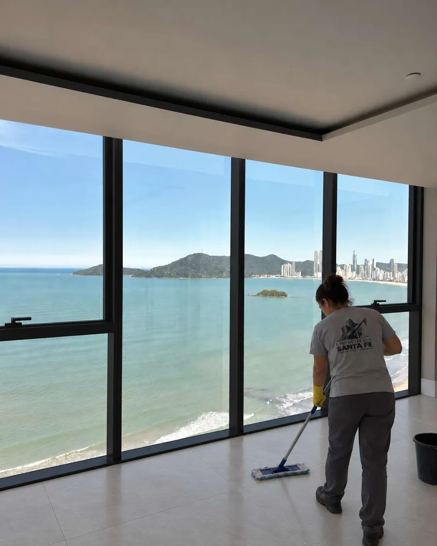 Colaboradora da Santa Fé na limpeza pós-obra de um apartamento entregue, com a orla de Balneário Camboriú pela janela